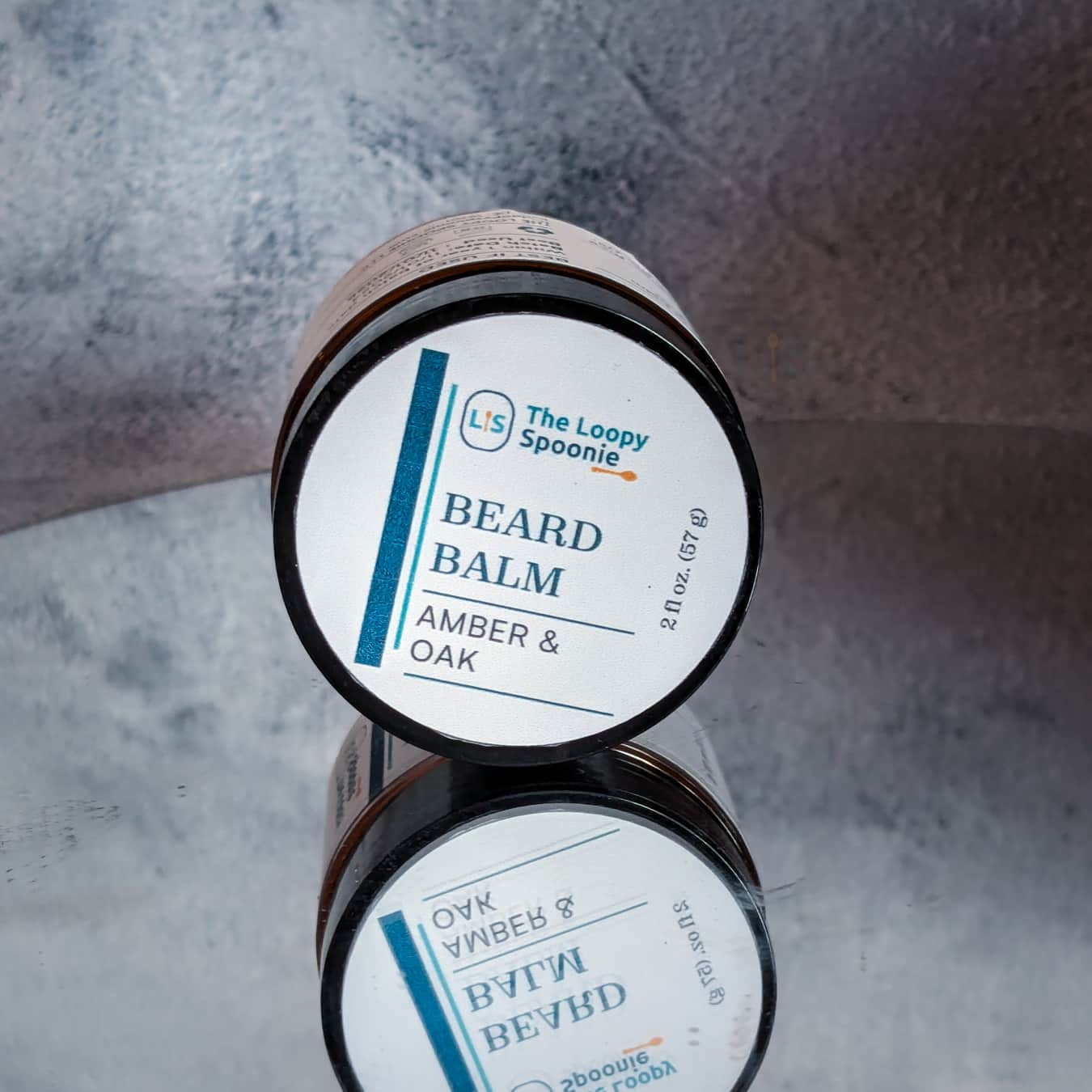 amber colored jar laying on its side the lid on. a label that says Beard Balm then Amber & Oak.