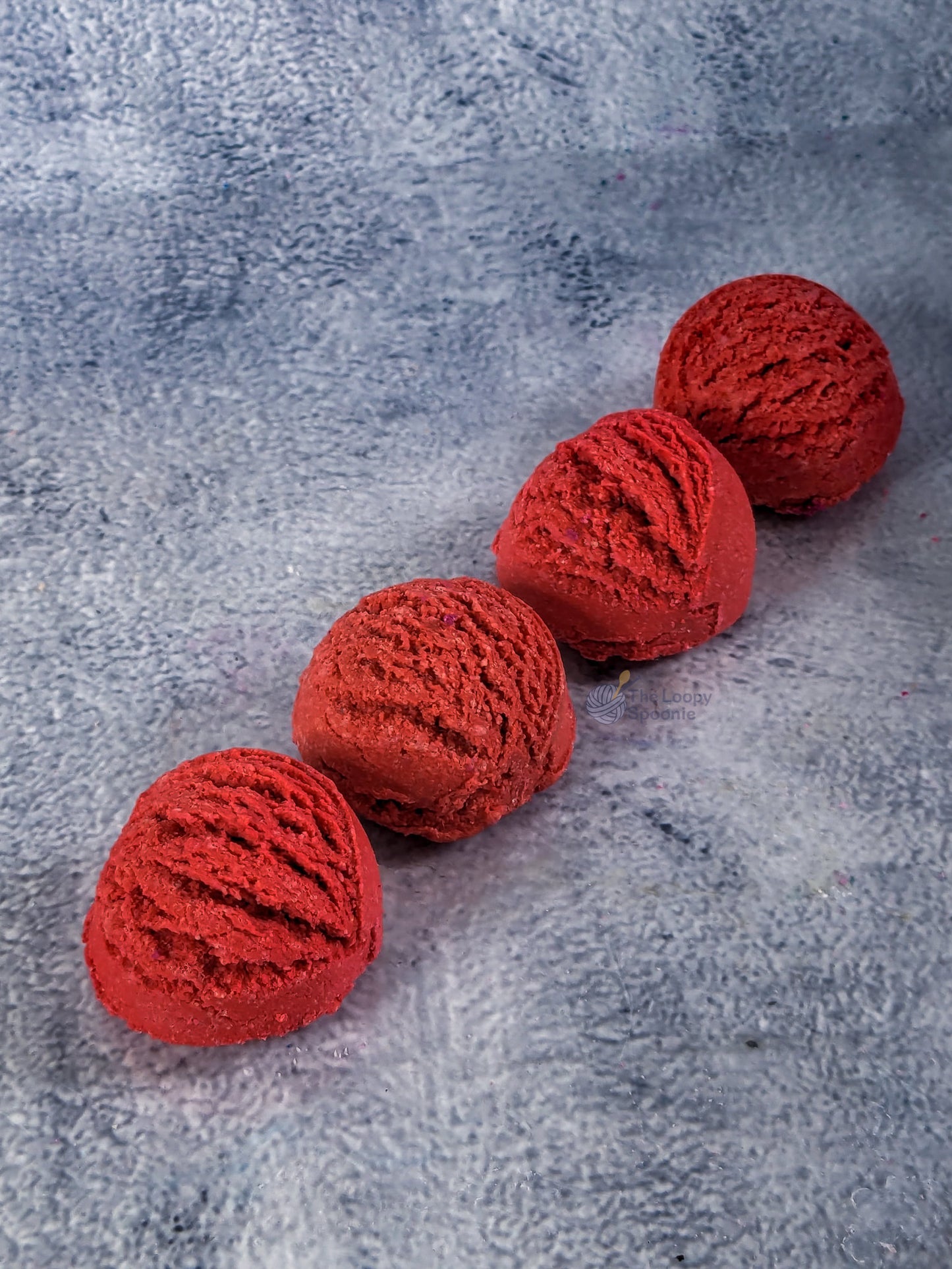 Four red mini bubble bath scoops placed diagonally on a grey textured background.