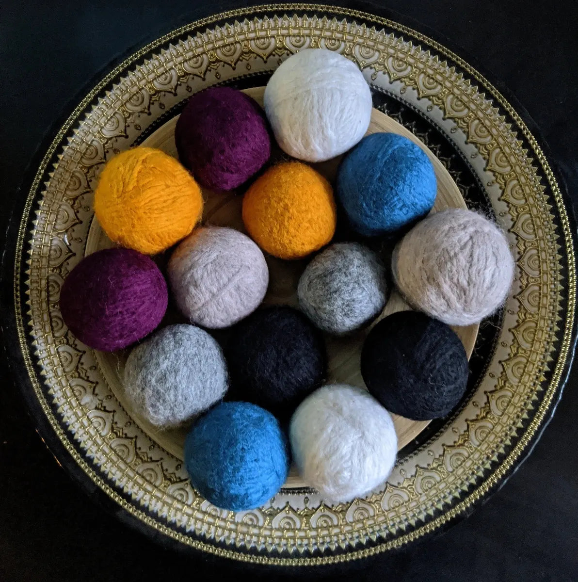 An ornate bowl filled with wool dryer balls in the colors: plum, blue, tan, cream, grey, and marigold 