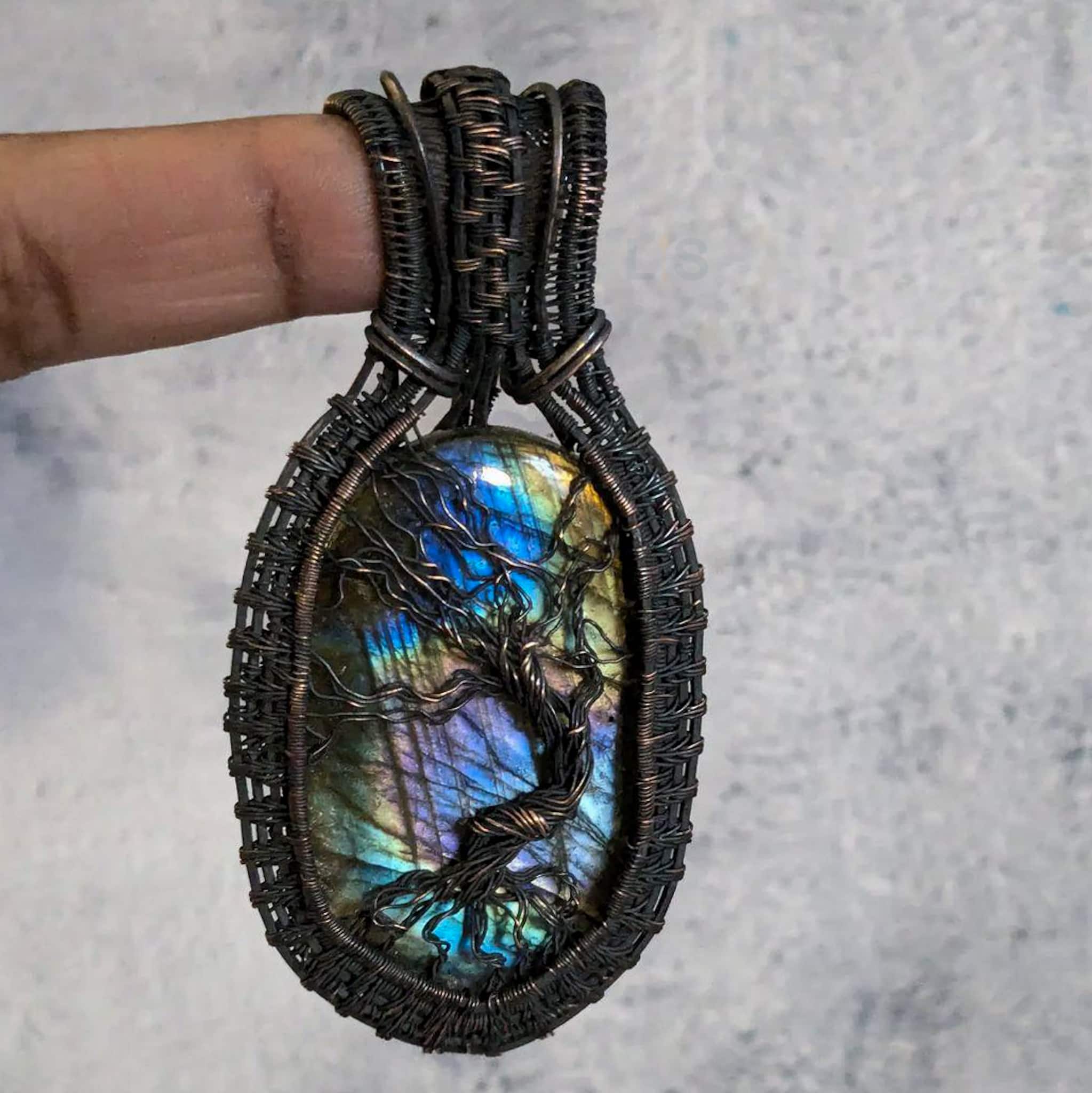 Multiolored large oval labradorite stone with copper wire tree over it and connecting to a copper wire woven frame. The copper wire has been antiqued to be dark brown with brighter copper highlights.