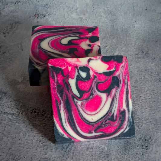 Two soap bars with swirls of neon pink, dark navy, and cream in a thick marble-like design are on a gray concrete background.