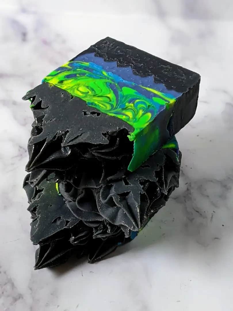 4 black, neon green & blue frosted soap bars stacked on a marble surface