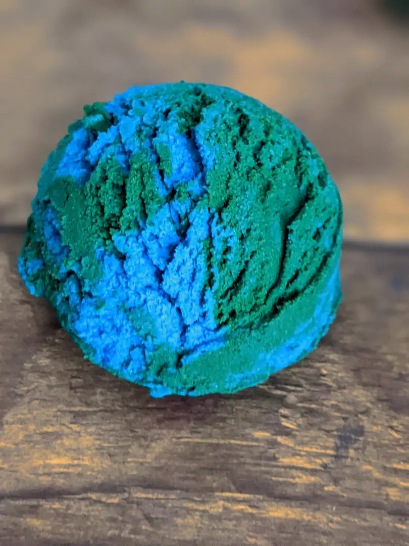 1 blue & green ocean themed solid bubble bath scoops placed on a wood grain background.