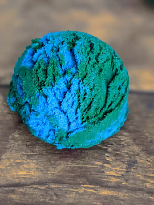 1 blue & green ocean themed solid bubble bath scoops placed on a wood grain background.