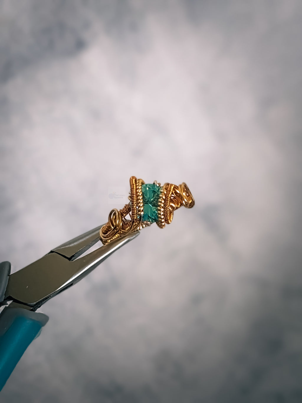 close up of a dual toned gold solitaire style wire wrapped ring featuring a faceted sky blue topaz gemstone.