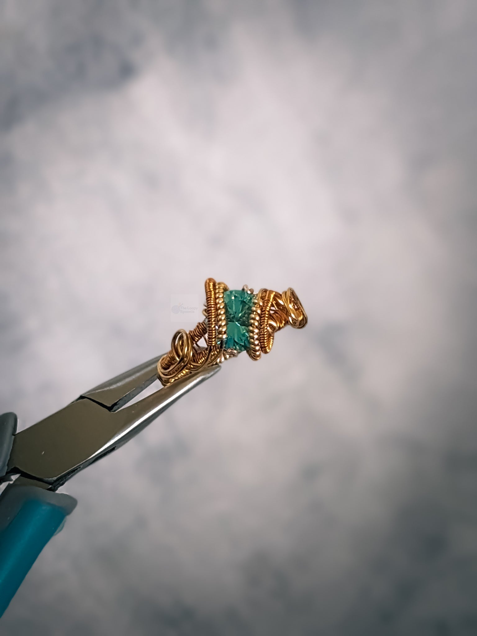close up of a dual toned gold solitaire style wire wrapped ring featuring a faceted sky blue topaz gemstone.