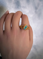 A hand wearing a bronze and gold wire wrap ring with a large sea blue cubic zirconia gem.