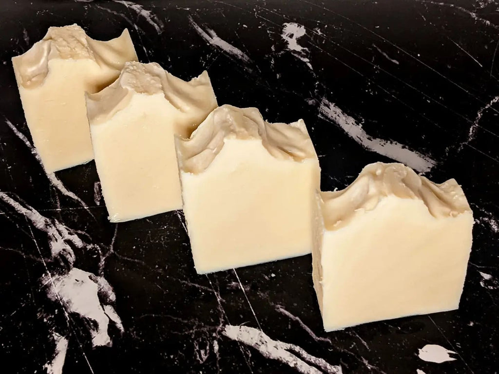 4 cream colored bars of handmade soap with textured tops, lined up diagonally on a black and white marble surface.