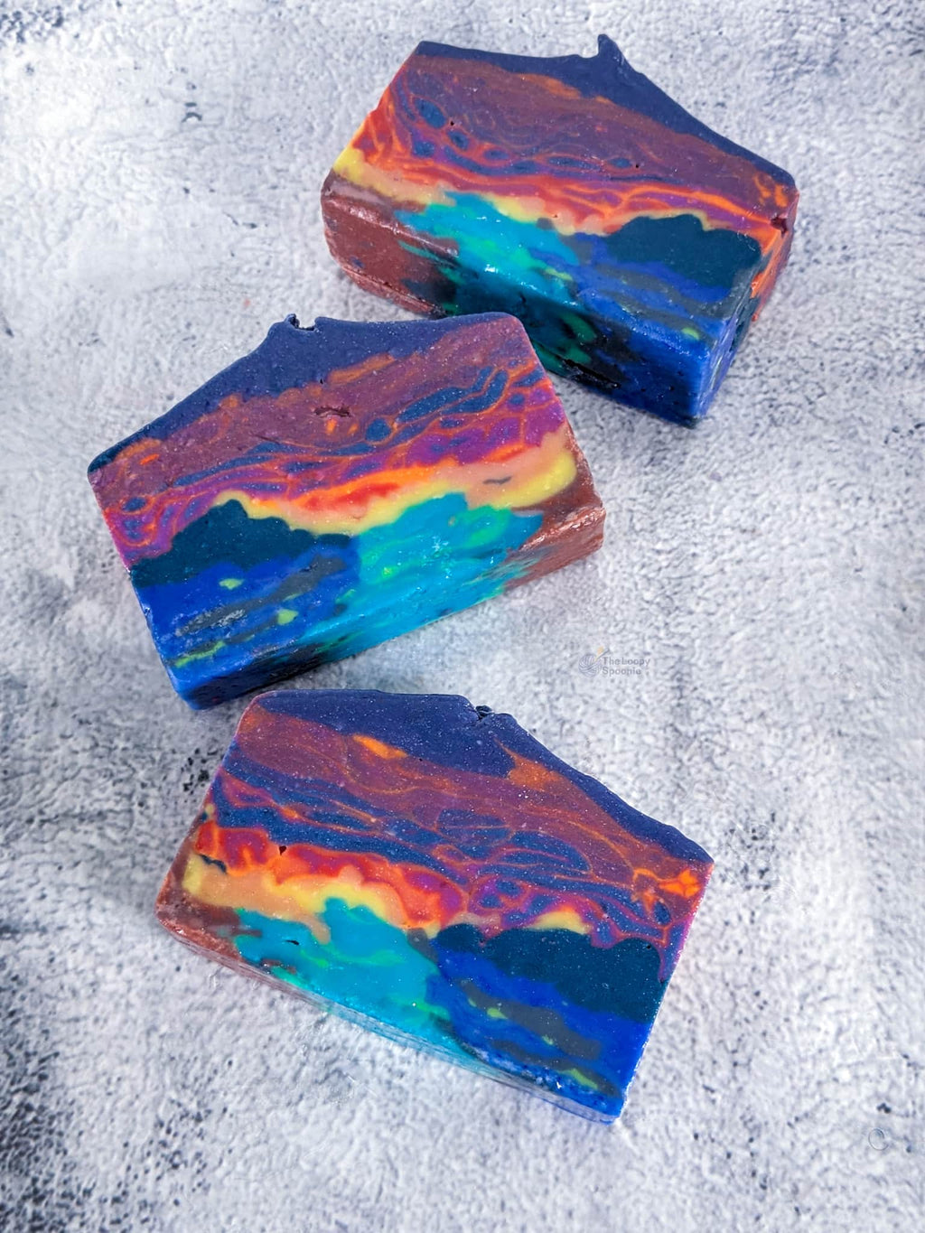 Three bars of soap designed to look like an abstract neon sunset over a vibrant blue/green ocean .