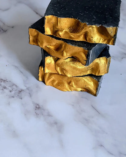 Vertical Stack of 4 black colored soaps with waves of shiny gold mica on the end of each soap.