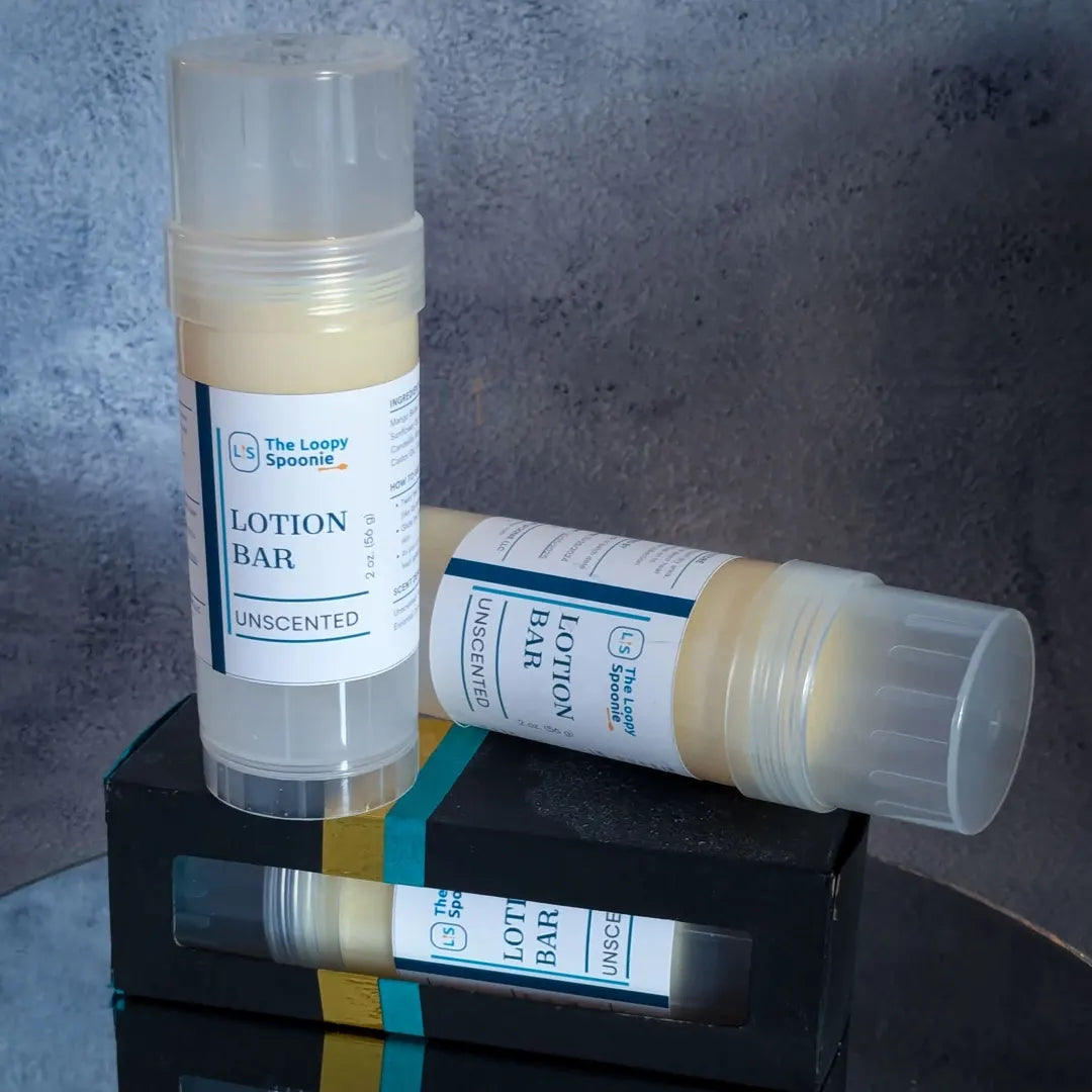 Two lotion bar tubes are on top of a lotion bar in a black box with another lotion bar visible in side. 

One lotion bar is upright, the second is behind and laying sideways on top of the boxed lotion bar