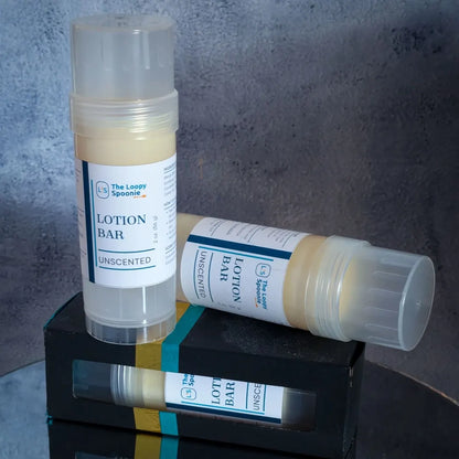 Two lotion bar tubes are on top of a lotion bar in a black box with another lotion bar visible in side. 

One lotion bar is upright, the second is behind and laying sideways on top of the boxed lotion bar