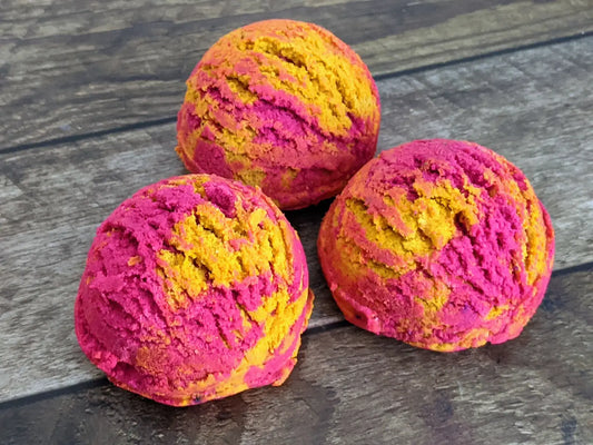 3 round solid bubble bath scoops with pink & yellow swirls, and placed on a wood grain background.