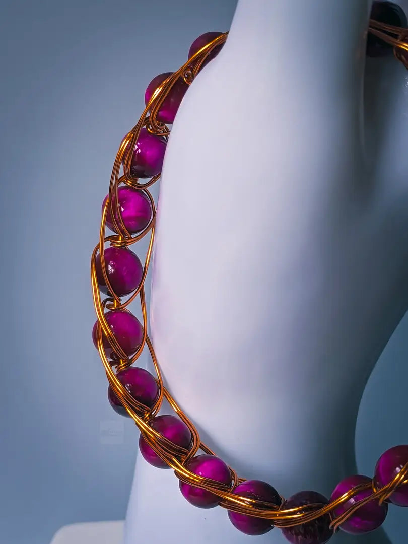 Close up of pink tiger eye beaded bracelet that's accented by bronze colored wire. 

The bracelet is displayed on the thumb of a white mannequin hand, and is in front of a light grey/blue background.