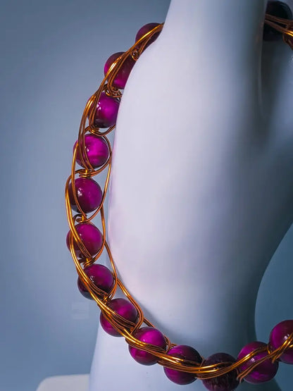Close up of pink tiger eye beaded bracelet that's accented by bronze colored wire. 

The bracelet is displayed on the thumb of a white mannequin hand, and is in front of a light grey/blue background.