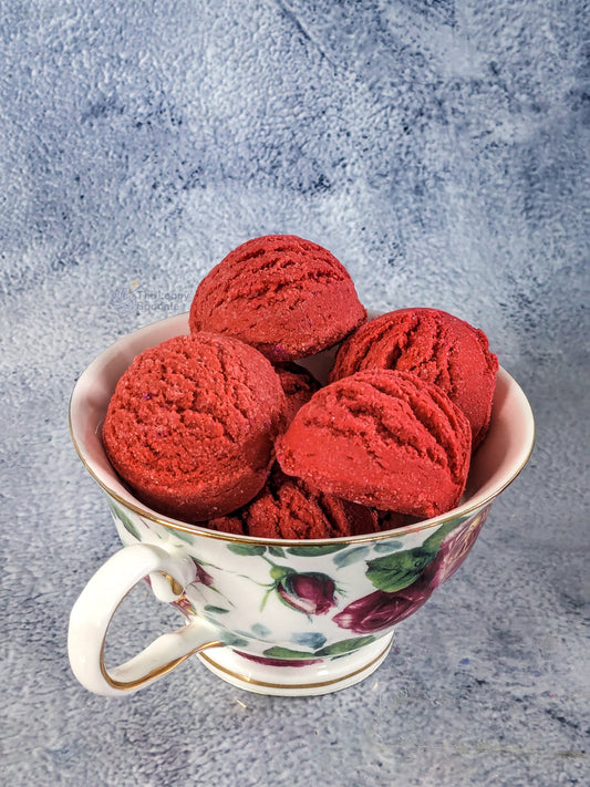 Several red strawberry scented mini bubble bath scoops in a floral teacup against a grey textured background.