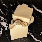 3 cream colored bar soaps stacked on top of each other with 1 soap upright in front of the stack. The soaps are on a black marble surface