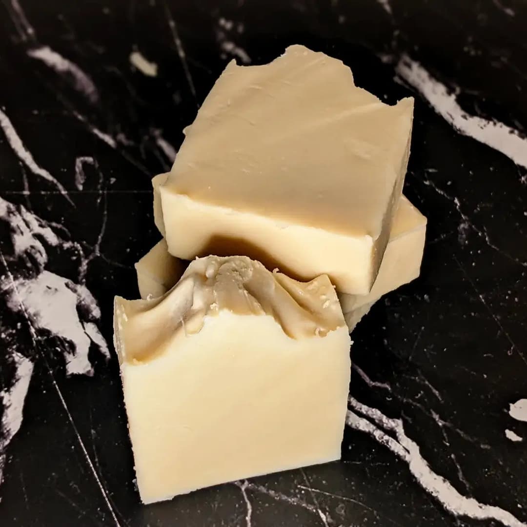 3 cream colored bar soaps stacked on top of each other with 1 soap upright in front of the stack. The soaps are on a black marble surface