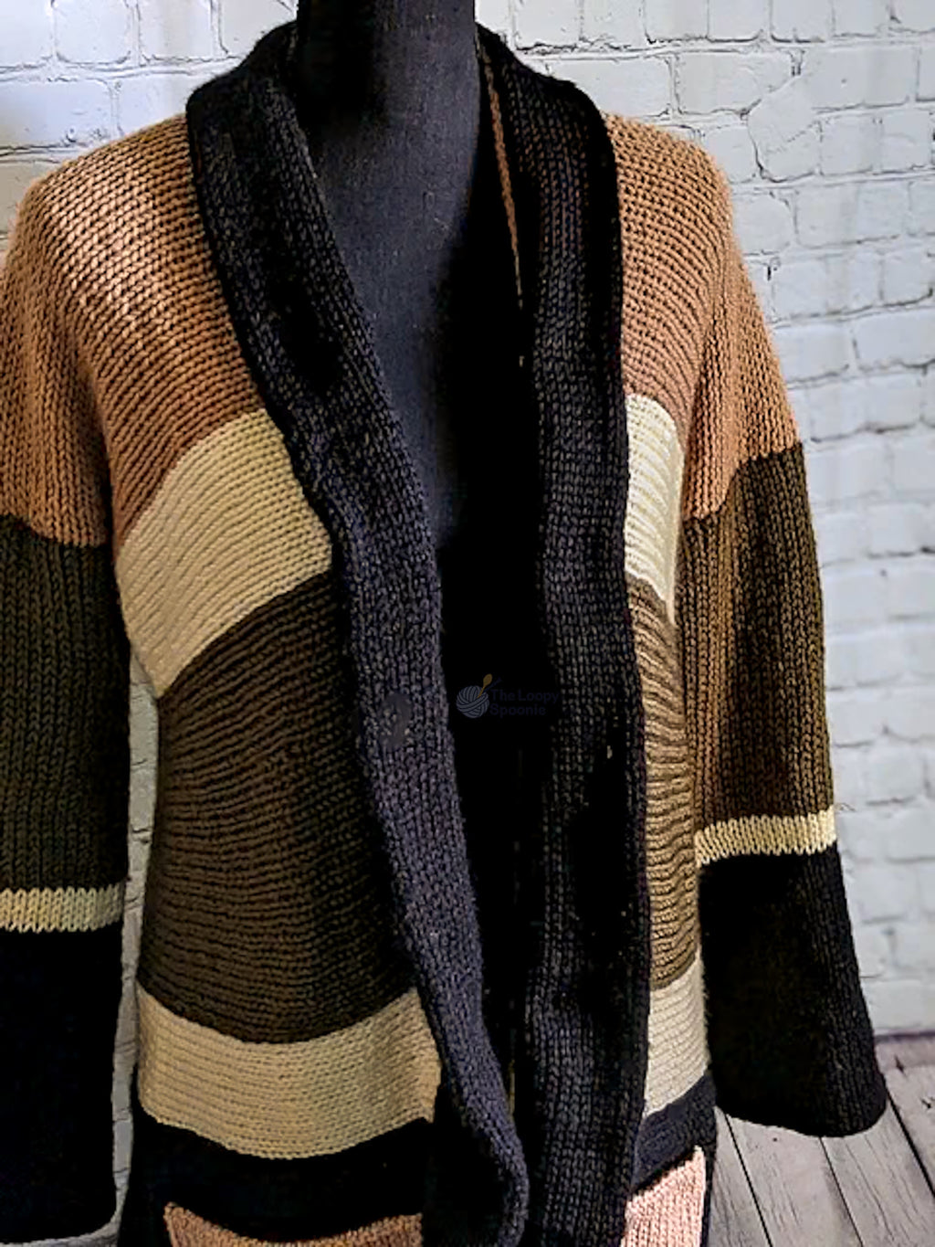 a knit cardigan with an, cream, olive green, and black stripes is pictured on a mannequin form in front of a white brick background
