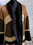 a knit cardigan with an, cream, olive green, and black stripes is pictured on a mannequin form in front of a white brick background