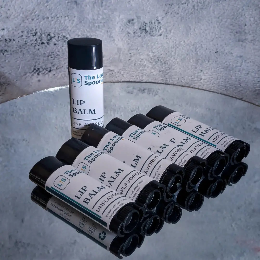 6 lip balms in oval tubes lay diagonally on a mirror. 1 tube is upright, showcasing a minimal label that says "Lip Balm".